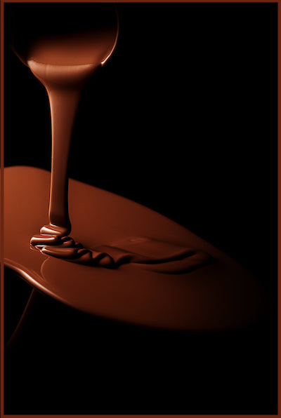 Artisanal chocolate being poured in elegant streams with warm lighting - capturing the pure essence of Delessa's chocolate craftsmanship